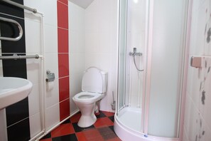 Un baño con inodoro blanco, lavamanos y ducha con mampara de vidrio.