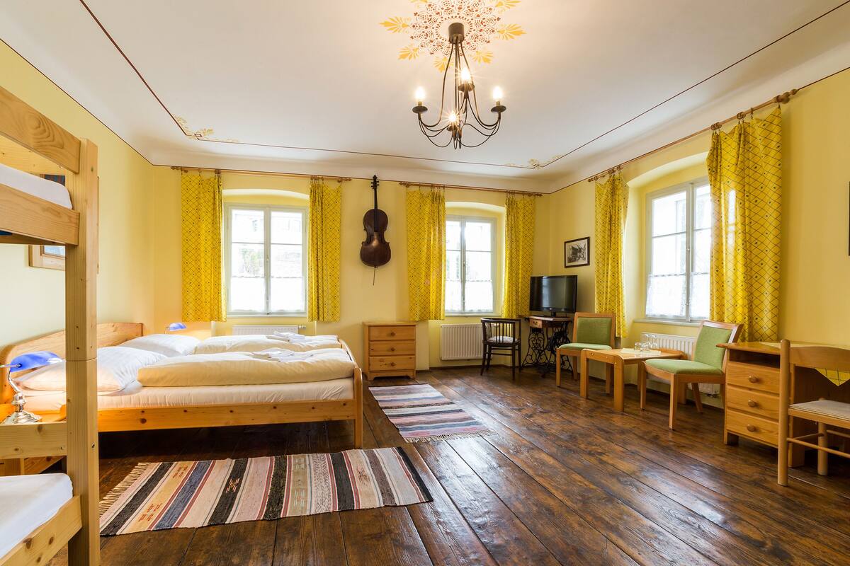 A room with a bunk bed, a desk with a chair, a television, and a violin hanging on the wall.