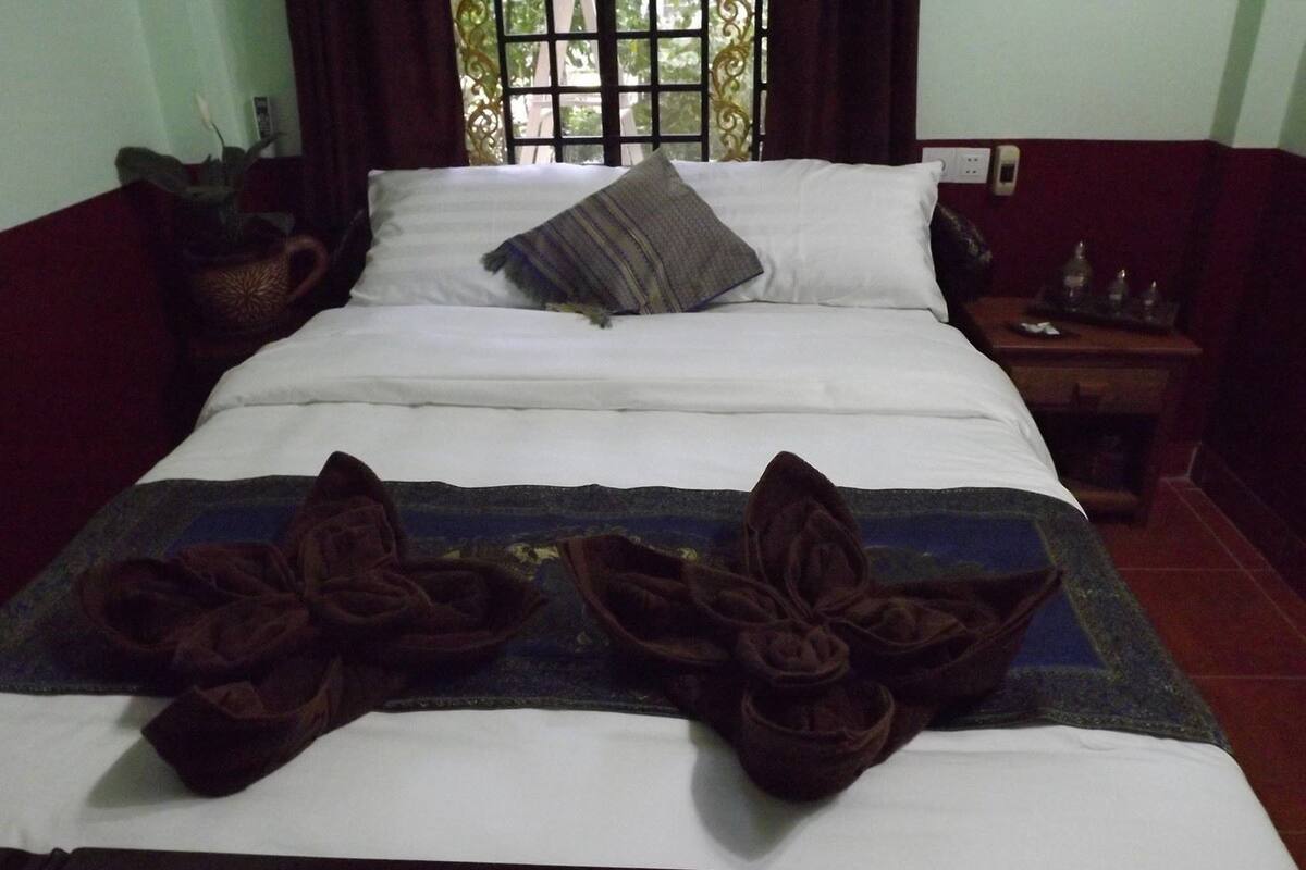 Una cama con una colcha blanca y azul, una almohada gris y un edredón marrón oscuro doblado en el centro.