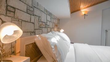 A bedroom with a stone wall, a bed with white bedding, a bedside lamp, and a wall-mounted light fixture.