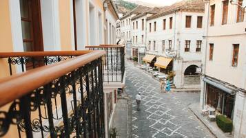A narrow cobblestone street with buildings on either side, a balcony with wrought iron railings, and a few people walking.