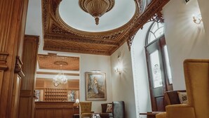 Eine luxuriöse Lobby mit einem prächtigen Kronleuchter, einem großen Gemälde und einem hölzernen Empfangsschalter.