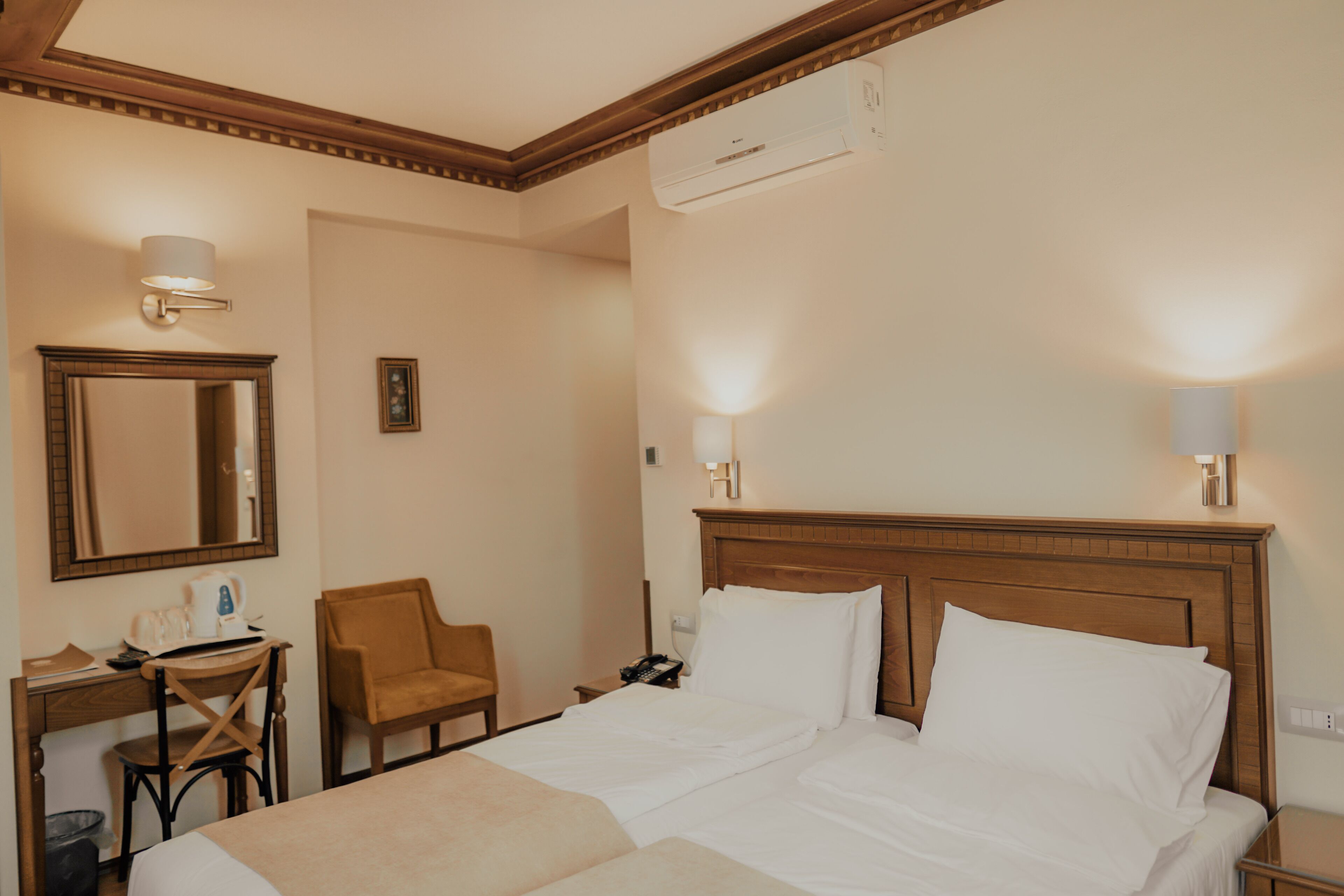 Una habitació d'hotel amb un llit gran, una taula de treball amb una cadira, un telèfon i un aire condicionat fixat a la paret.