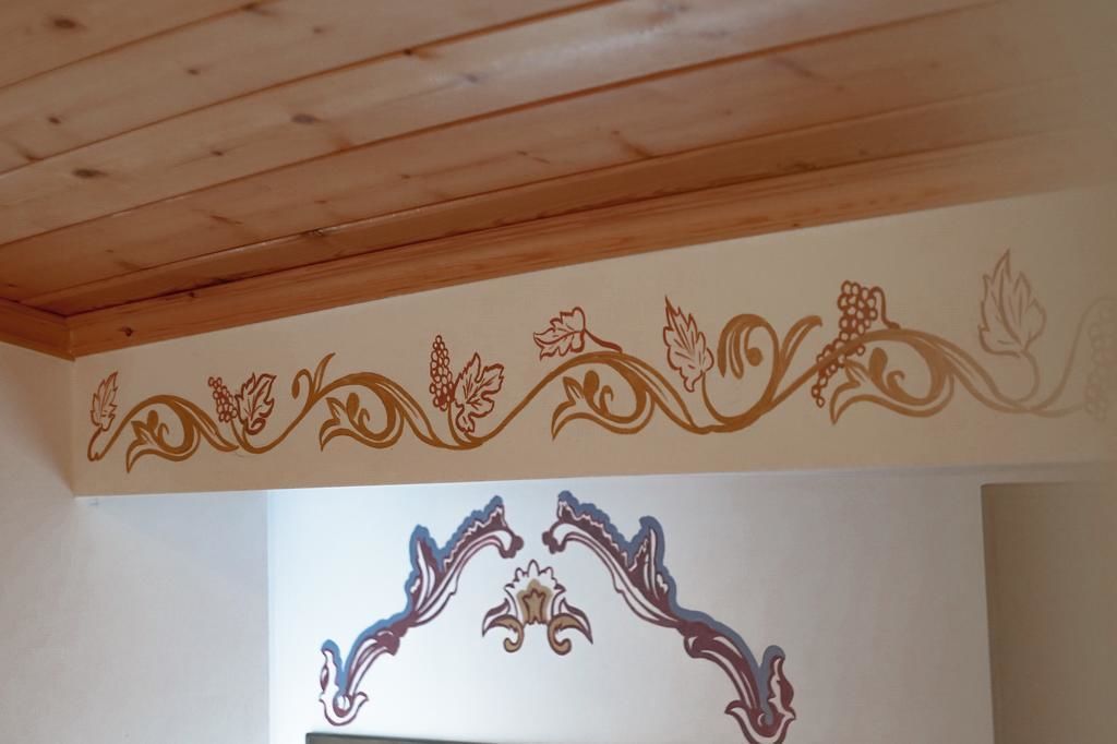 A ceiling with a wooden beam structure and decorative wall patterns including floral and grapevine designs.