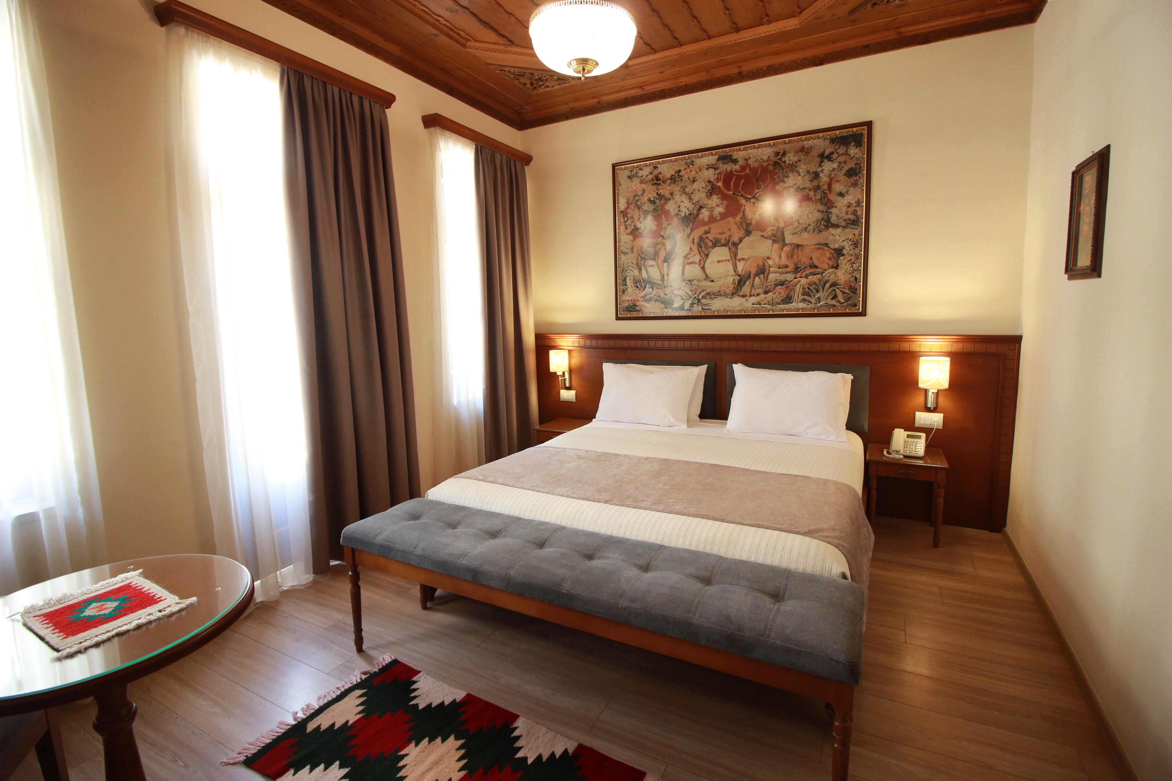 Habitación de hotel con una cama grande, una mesita de noche, un teléfono, un cuadro en la pared y una ventana con cortinas.