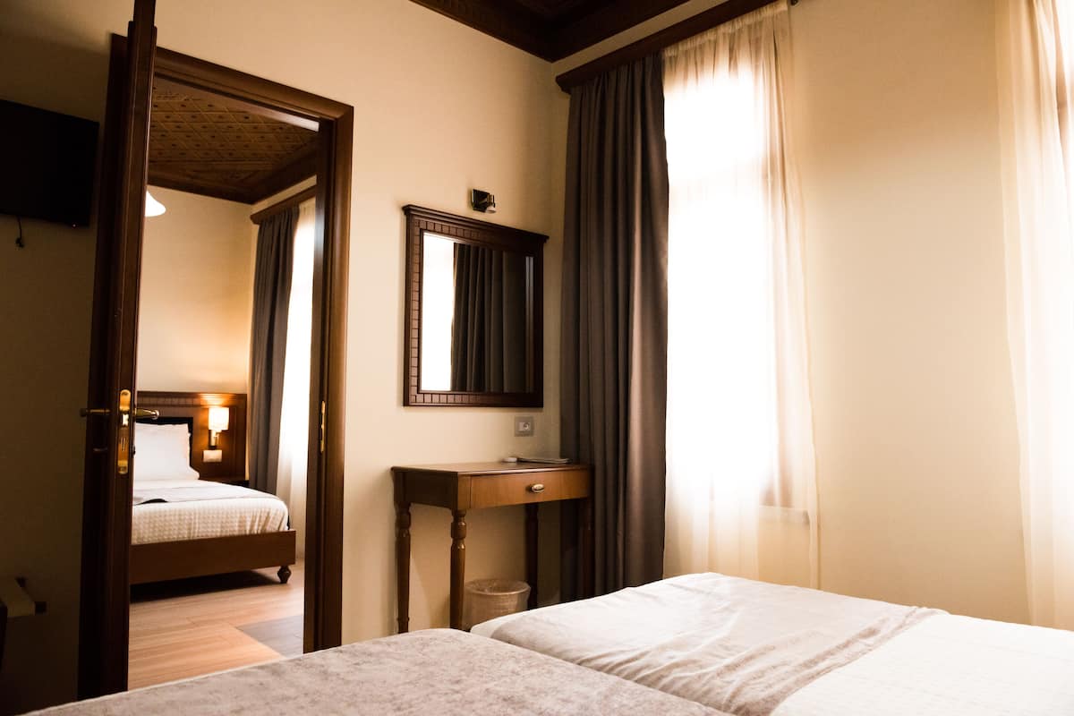 A hotel room with a bed, a bedside table, a mirror, and a window with curtains.
