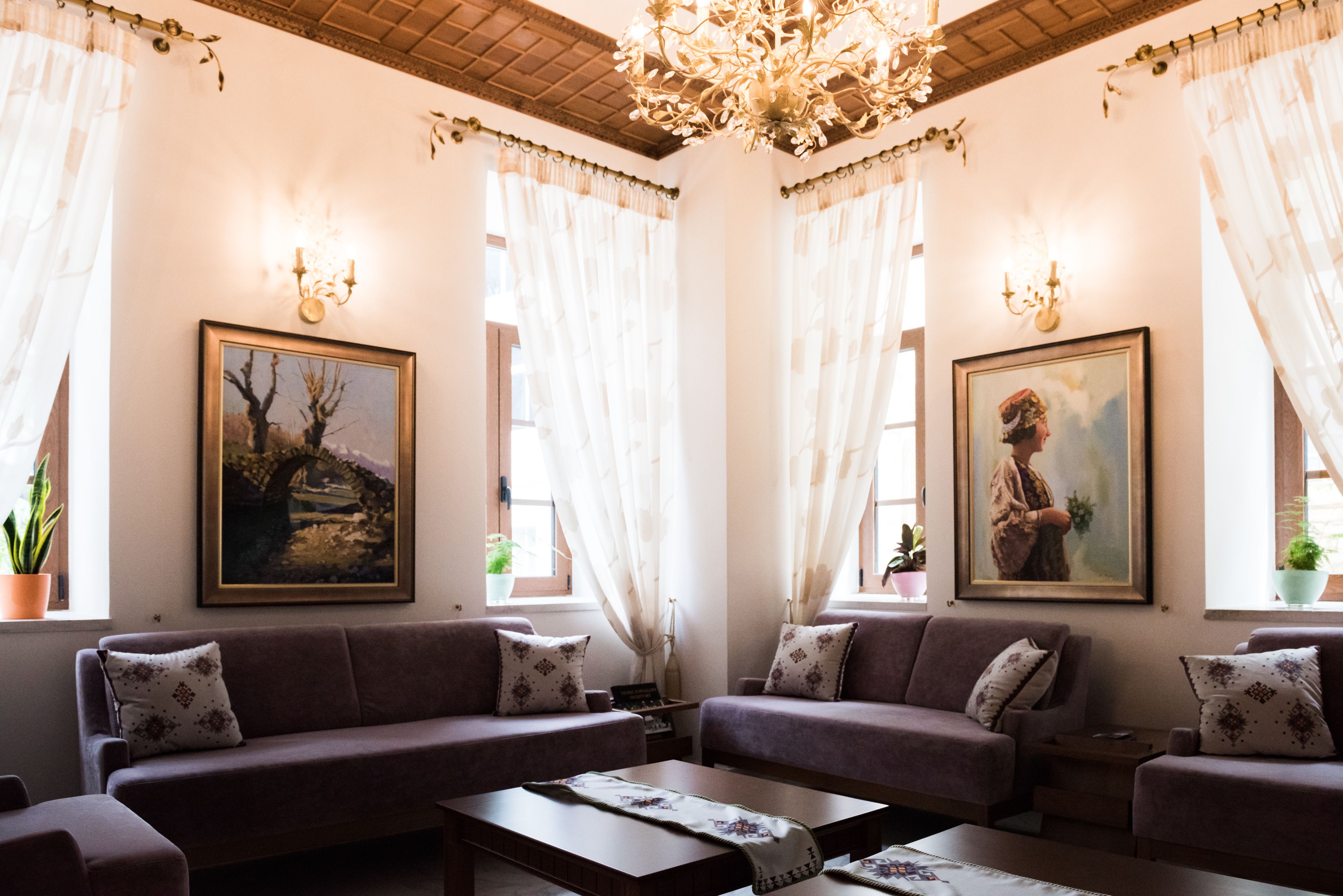 Une pièce comprenant deux canapés, une table basse et un lustre. Deux tableaux ornent les murs, et une fenêtre est agrémentée de rideaux.