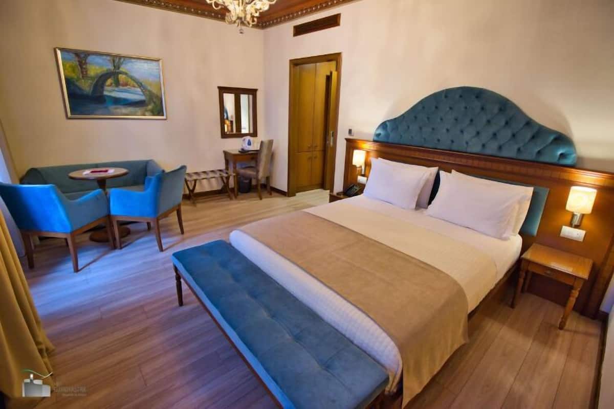 A hotel room with a large bed, a desk, a chair, a bench, and a painting on the wall.