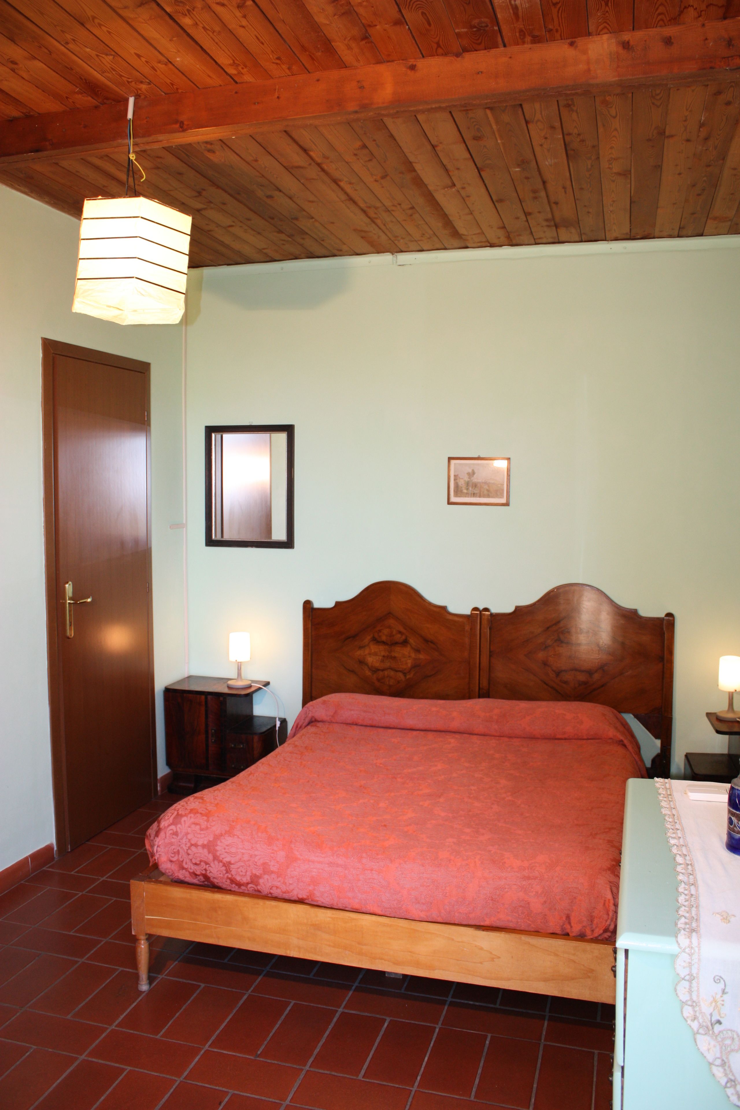 Ein Schlafzimmer mit einem hölzernen Bett, einem Nachttisch mit Lampe, einem gerahmten Bild an der Wand und einer Holzboden.