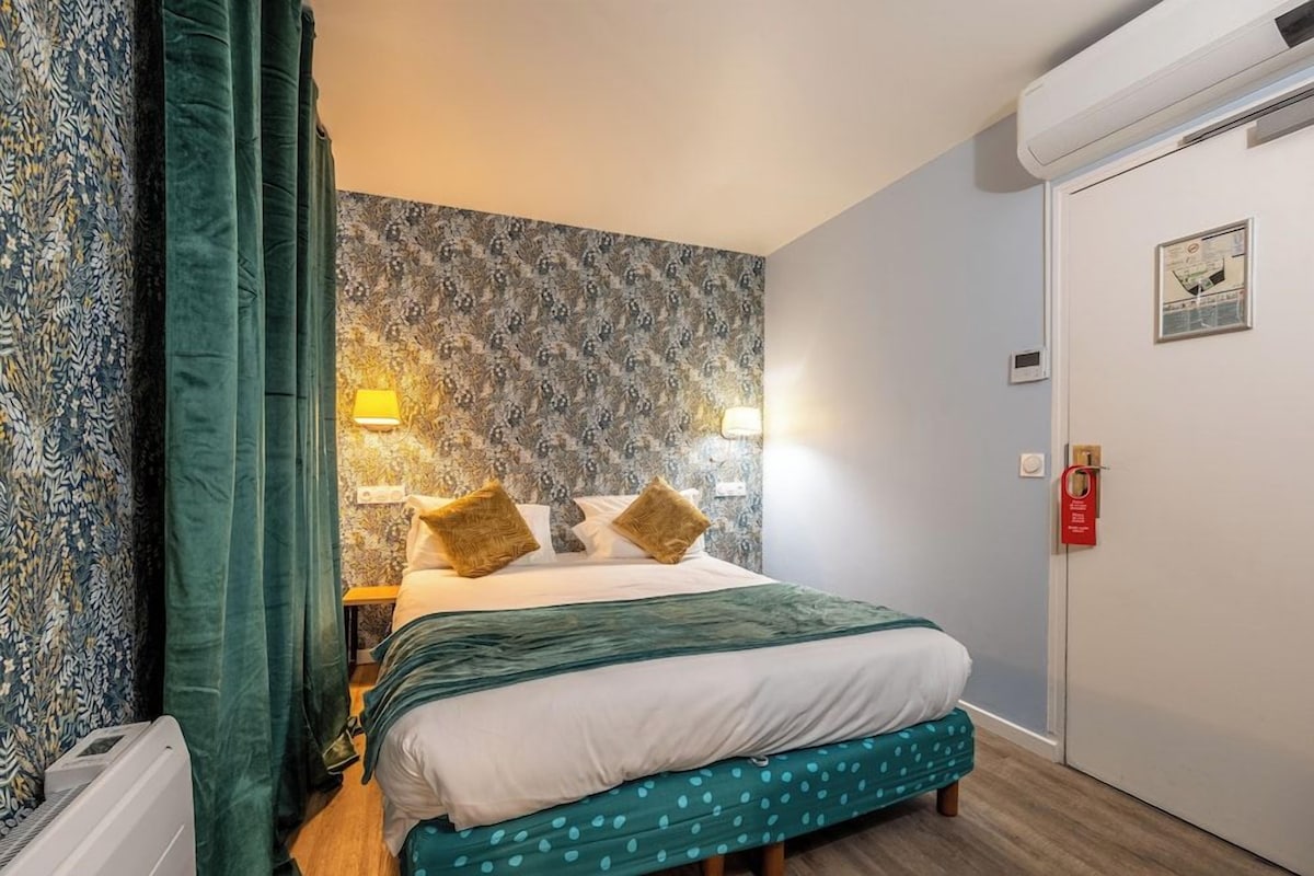 Une chambre d’hôtel avec un lit, une table de chevet, une lampe, un mur décoré d’un motif et une porte avec une serrure.