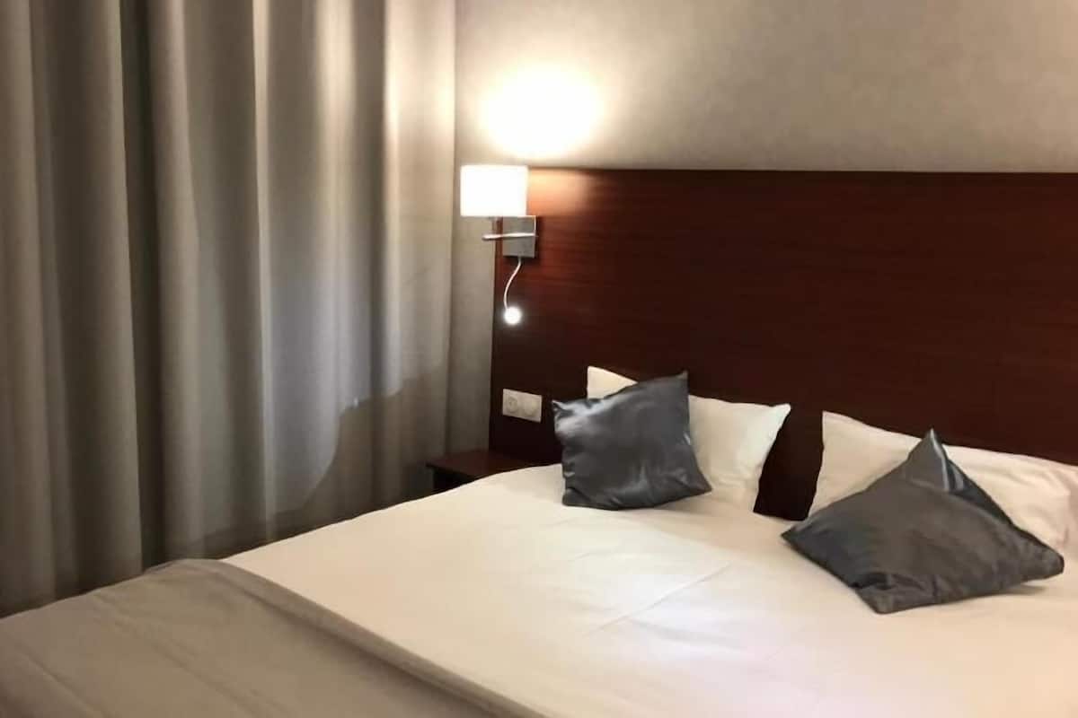 Ett hotellrum med en säng, gardiner, ett nattduksbord och en vägglampa.