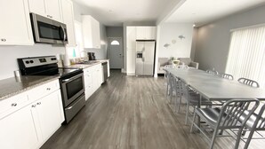 A modern kitchen with white cabinets, stainless steel appliances, and a dining area with a long table and chairs. - 140 S. Monroe St., Watkins Glen (Watkins Glen)
