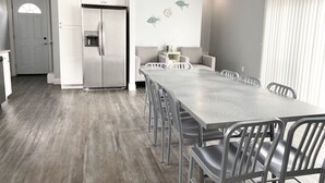 A modern kitchen with white cabinets, a stainless steel refrigerator, and a dining area with a long table and chairs. - 140 S. Monroe St., Watkins Glen (Watkins Glen)