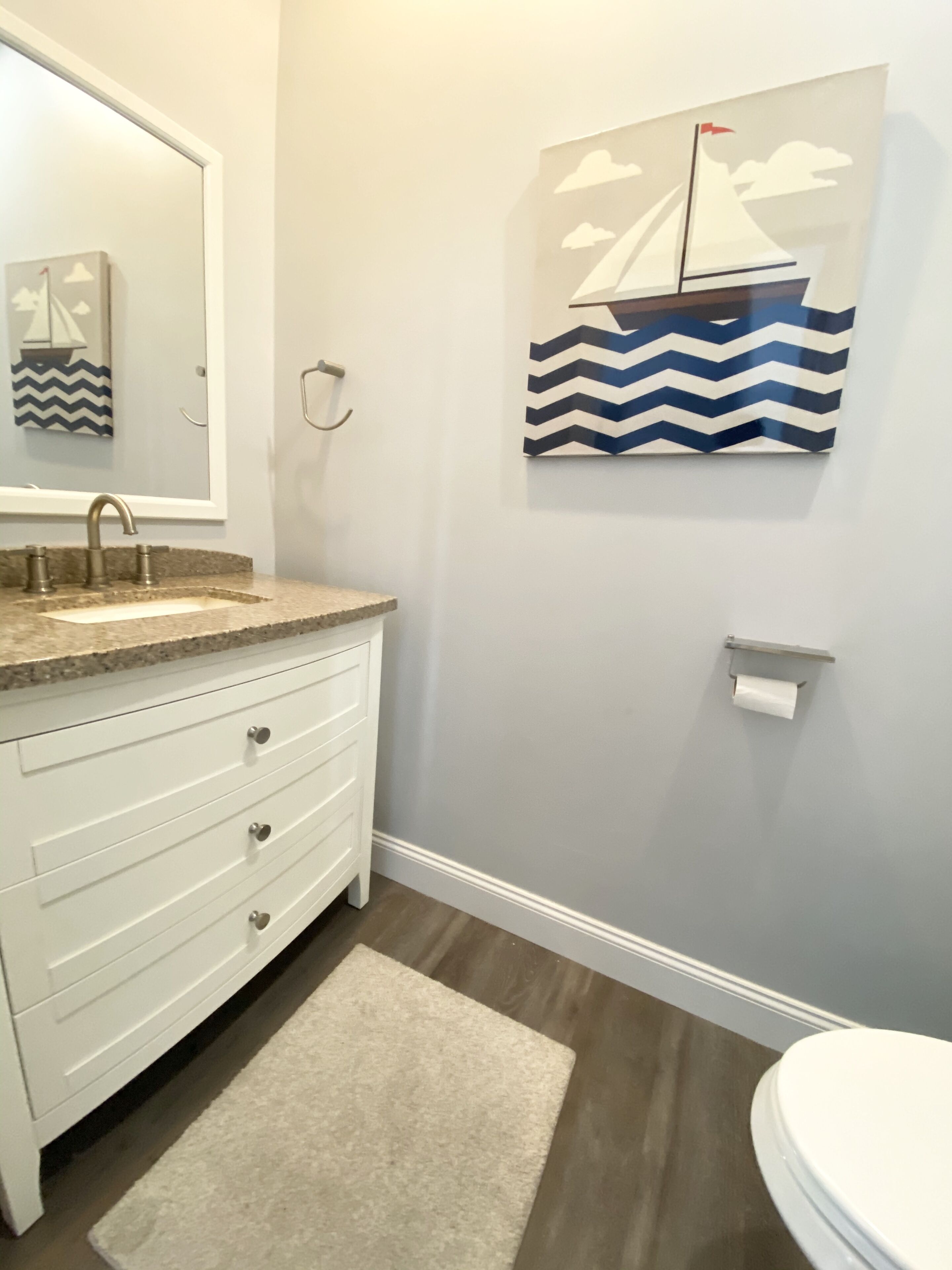 A bathroom with a white vanity, a sink, a mirror, a toilet, and a wall-mounted towel rack.