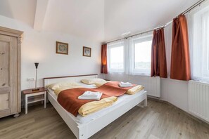 A bedroom with a bed, nightstand, wardrobe, and windows with curtains. - Villa Gardena (Cesky Krumlov)