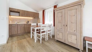 A compact kitchen with wooden cabinets, a white dining table, and a large wardrobe. - Villa Gardena (Cesky Krumlov)