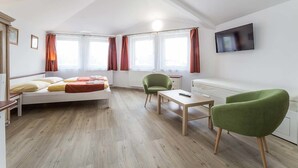 A modern, well-lit room with a bed, two green chairs, a small table, and a TV on the wall. - Villa Gardena (Cesky Krumlov)