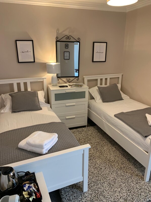 A hotel room with two beds, a bedside table with a lamp, a mirror, and framed pictures on the wall.