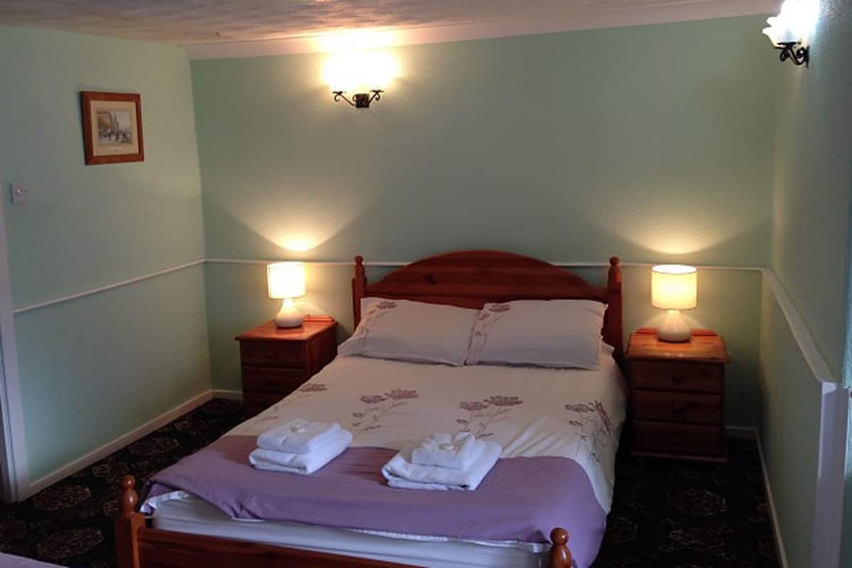 Una cama bien hecha con dos mesitas de noche, cada una con una lámpara, en una habitación con paredes verde claro y un cuadro en la pared.