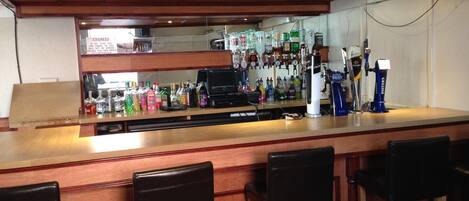 A bar area with wooden bar stools, a counter with various bottles, and a cash register.