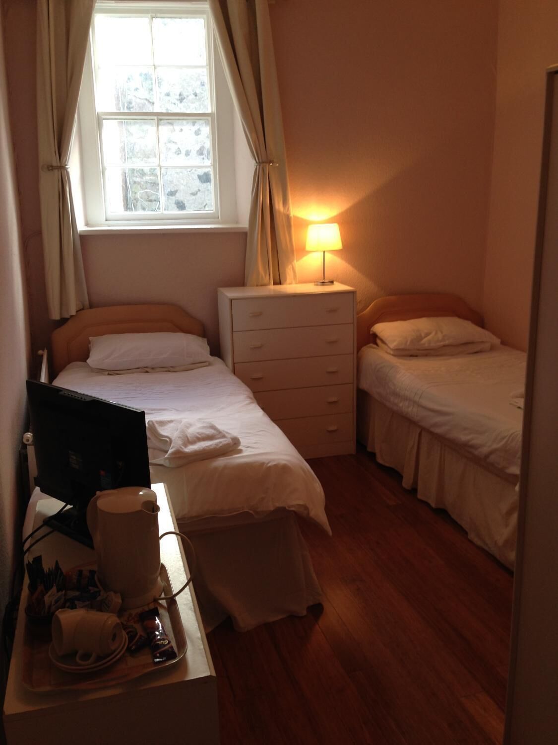 Een kleine, net kamer met een enkel bed, een bureau met een computer en een bedlampje.