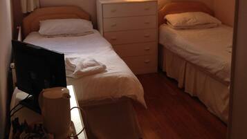 A small, tidy room with a single bed, a desk with a computer, and a bedside lamp.