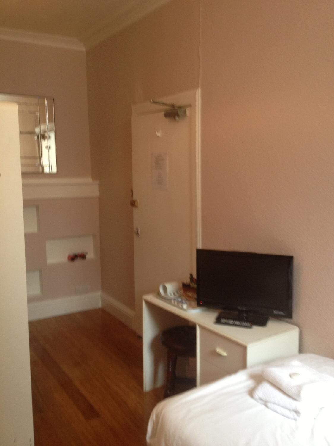 A hotel room with a bed, a desk with a TV, a mirror, and a door.