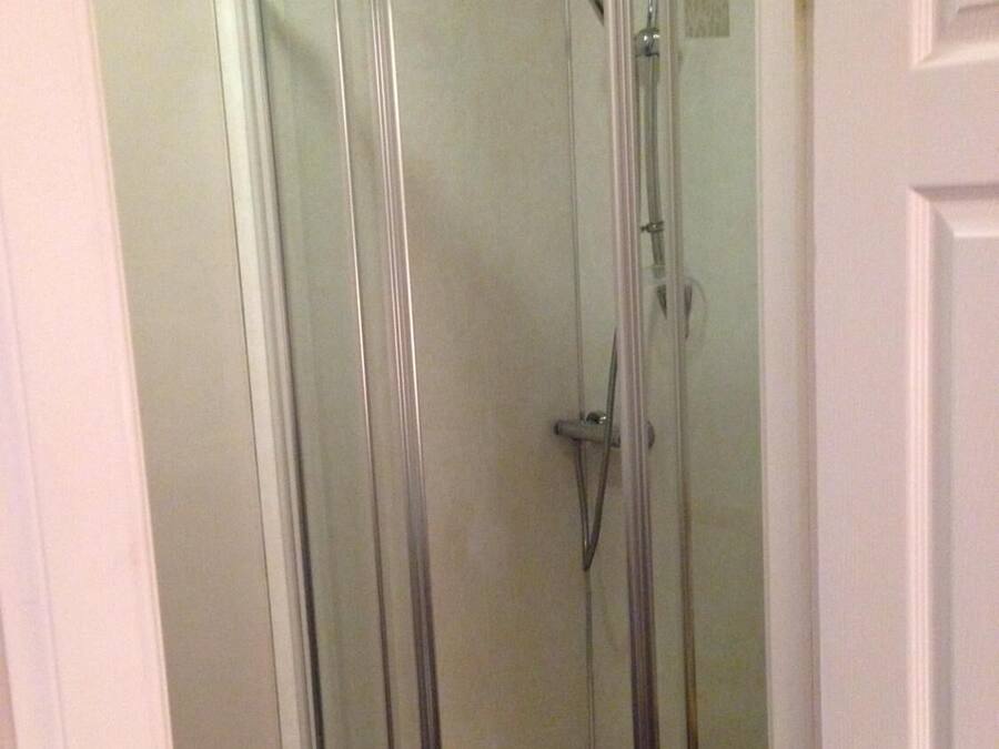 Une cabine de douche fermée par des parois en verre, équipée d’un pommeau de douche et d’un flexible de douche.