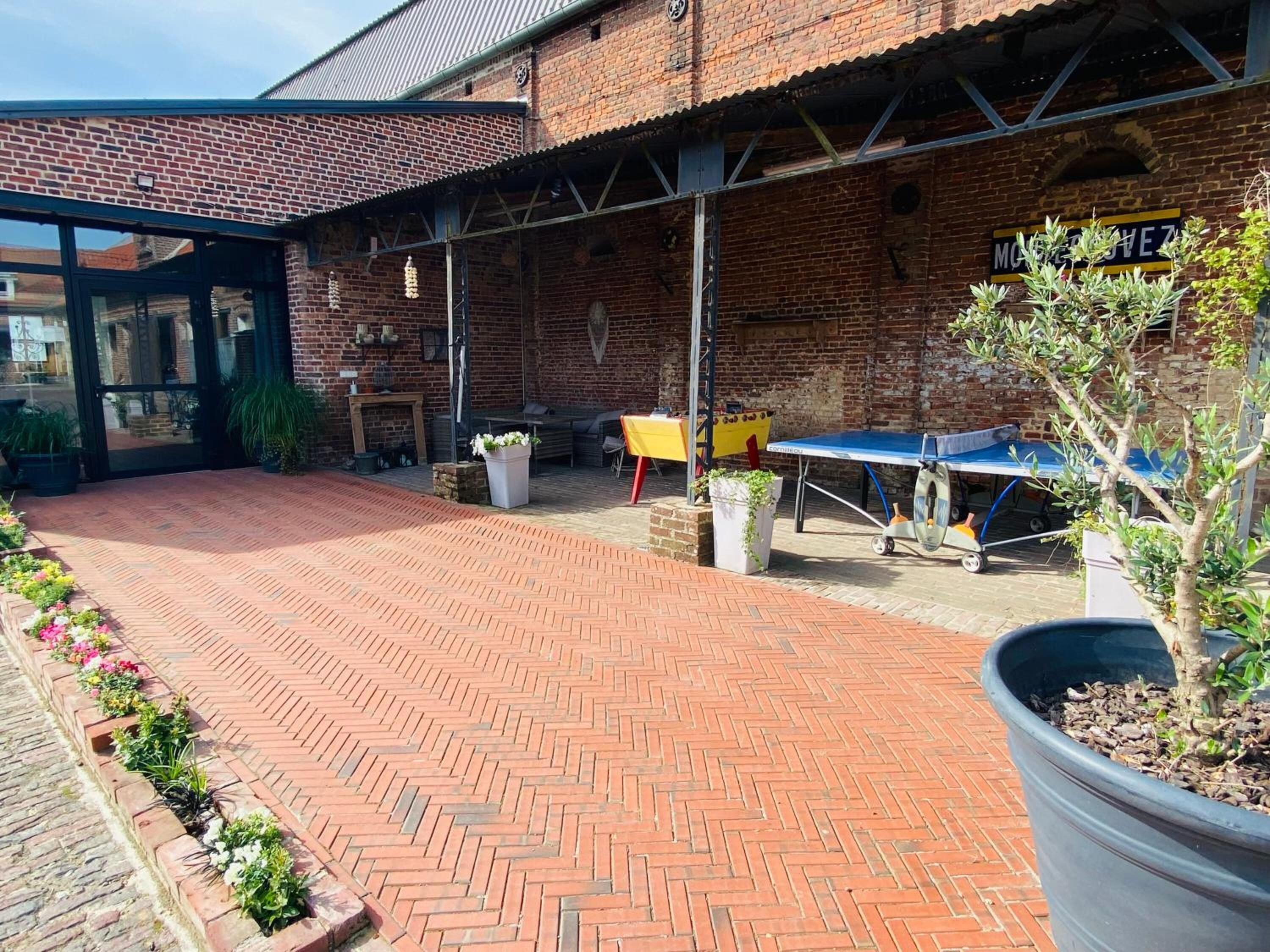 An outdoor patio area with a brick floor, outdoor seating, and a ping pong table.
