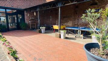 An outdoor patio area with a brick floor, outdoor seating, and a ping pong table.