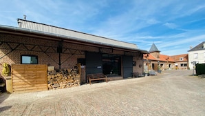 Een gebouw van baksteen met een metalen dak, een houtstapel en een houten omheining.