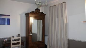 Ein Schlafzimmer mit einem hölzernen Kleiderschrank, einem Sessel, einem Bett, einem Spiegel, einer Chandelier und einem Fenster mit Vorhängen.