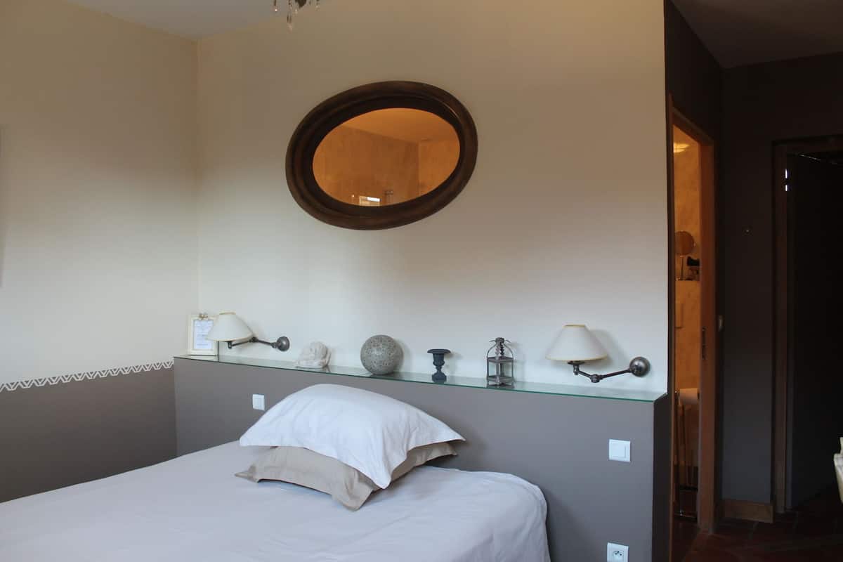 Een slaapkamer met een bed, een spiegel en een plank met decoratieve objecten.