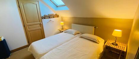 Un dormitorio con tragaluz, una cama, una mesita de noche con lámpara y un radiador.