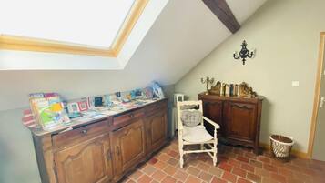 Una habitación con techo inclinado, tragaluz, escritorio de madera con libros, una silla blanca y un mueble pequeño.