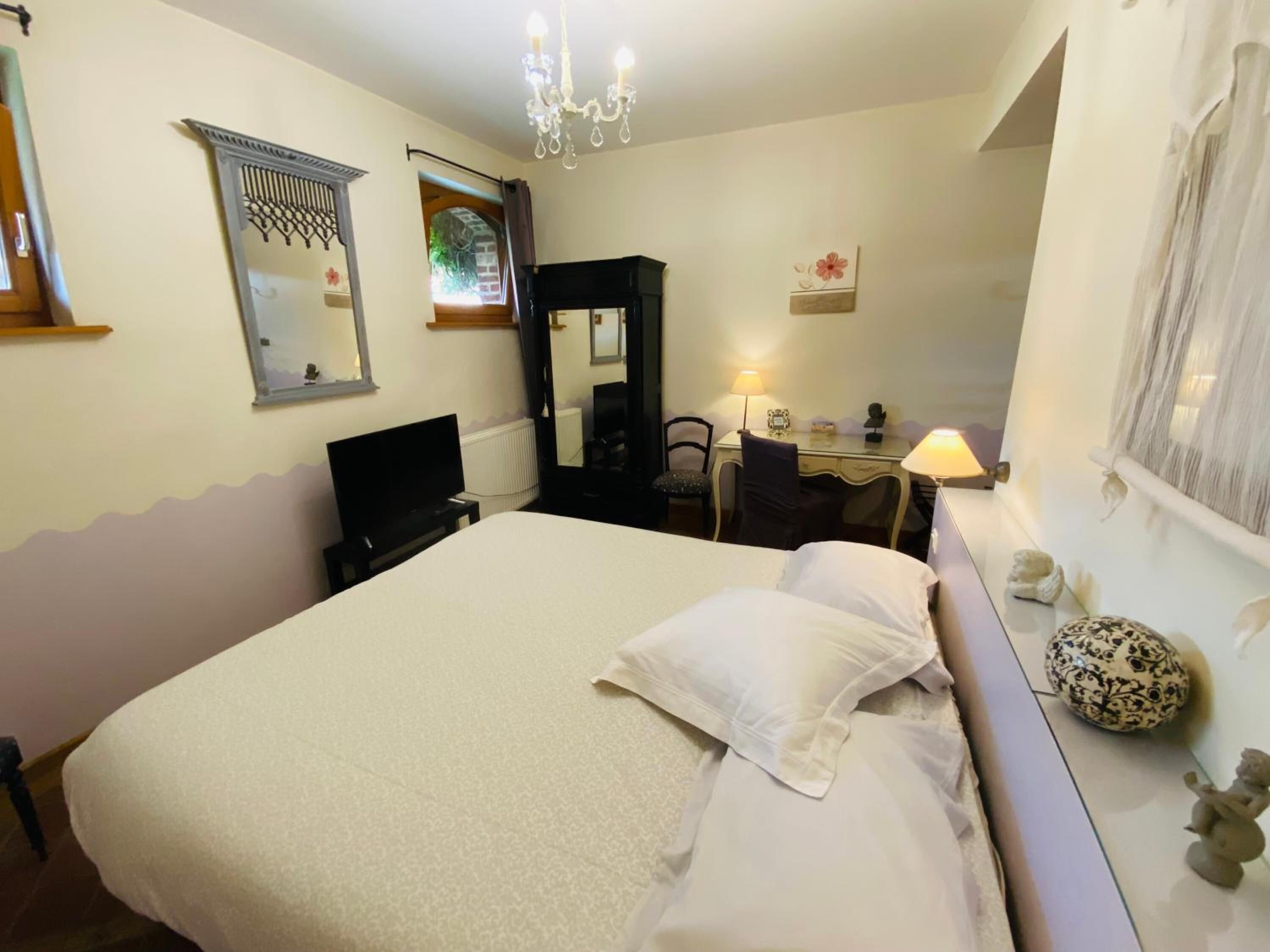 Una camera d'albergo con un letto grande, una scrivania, una sedia, una televisione e un lampadario.