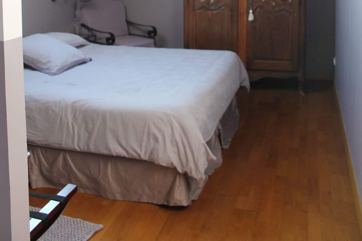 Een slaapkamer met een schuine kap, een bed, een houten garderobe en een stoel.