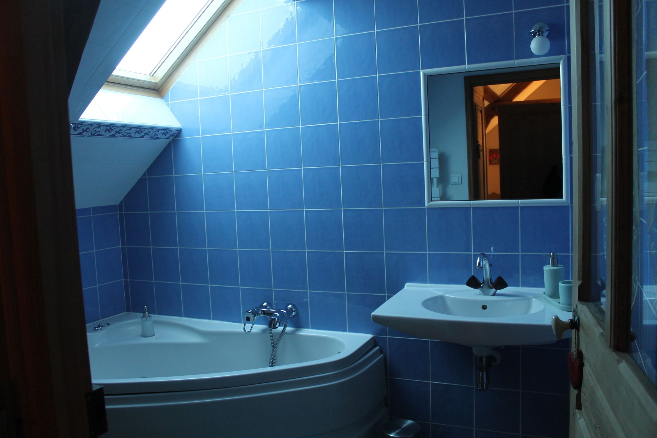 Un baño con azulejos azules, un tragaluz, una bañera y un lavabo.