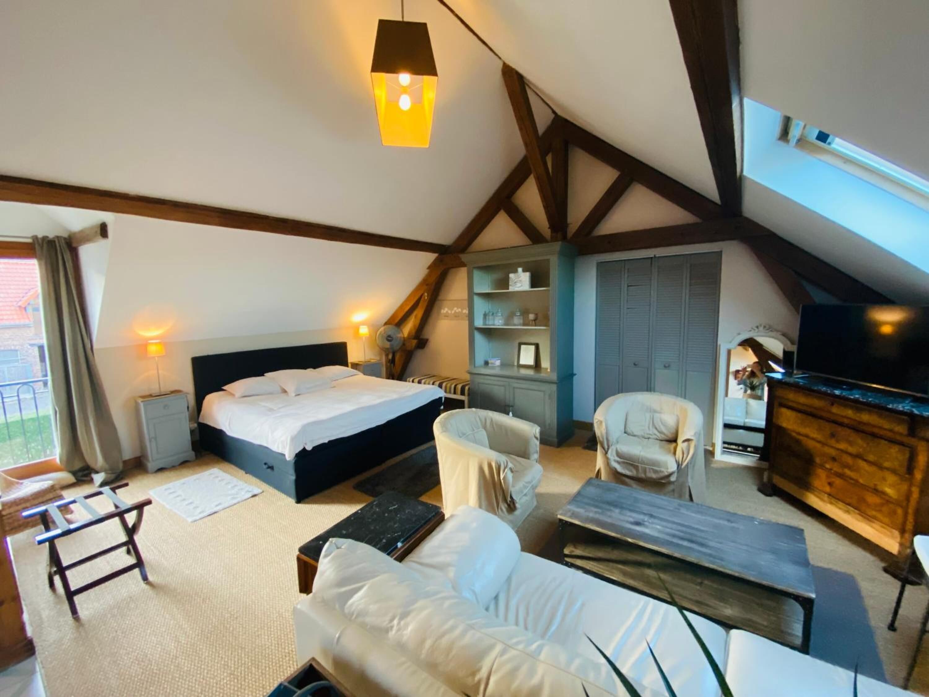 Ein gemütliches Schlafzimmer mit Bett, Sofa, Sessel, Schreibtisch und Fernseher.