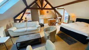 Een gezellige, goed verlichte zolderkamer met een groot bed, een slaapbank en een eettafel.