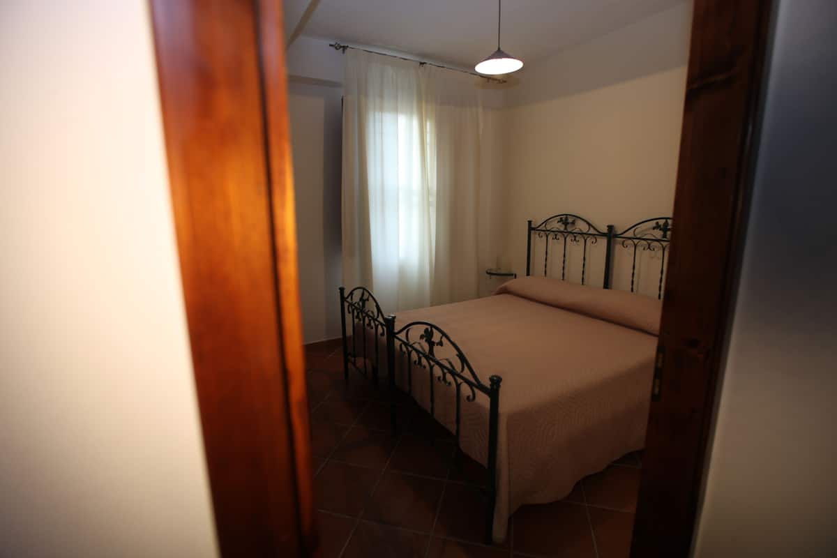 Een slaapkamer met een bed, gordijnen en een hanglamp.