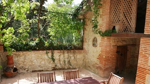 An outdoor patio with a wooden table and chairs, surrounded by a stone wall and greenery. - Le Farat (Auvillar)