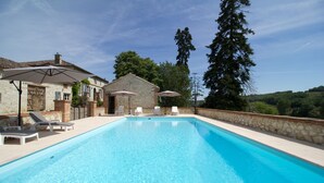 A swimming pool with lounge chairs and umbrellas, surrounded by stone walls and a stone building. - Le Farat (Auvillar)