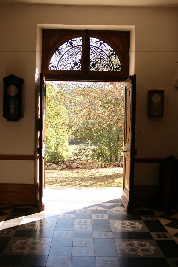 Una puerta abierta que da a un jardín con suelo de baldosas y un reloj en la pared.