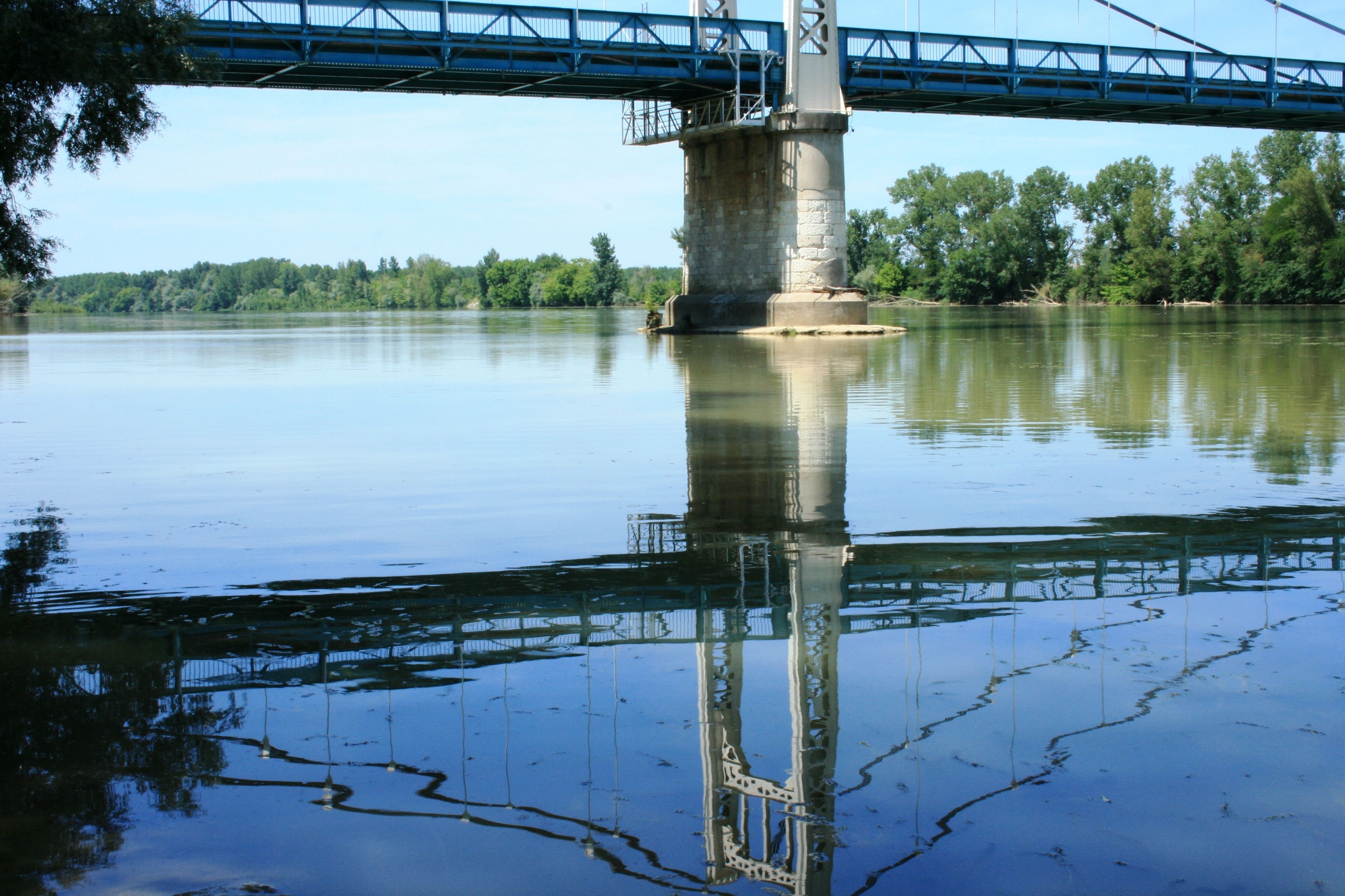 Un puente sobre un río tranquilo, reflejando el puente y los árboles en el agua.