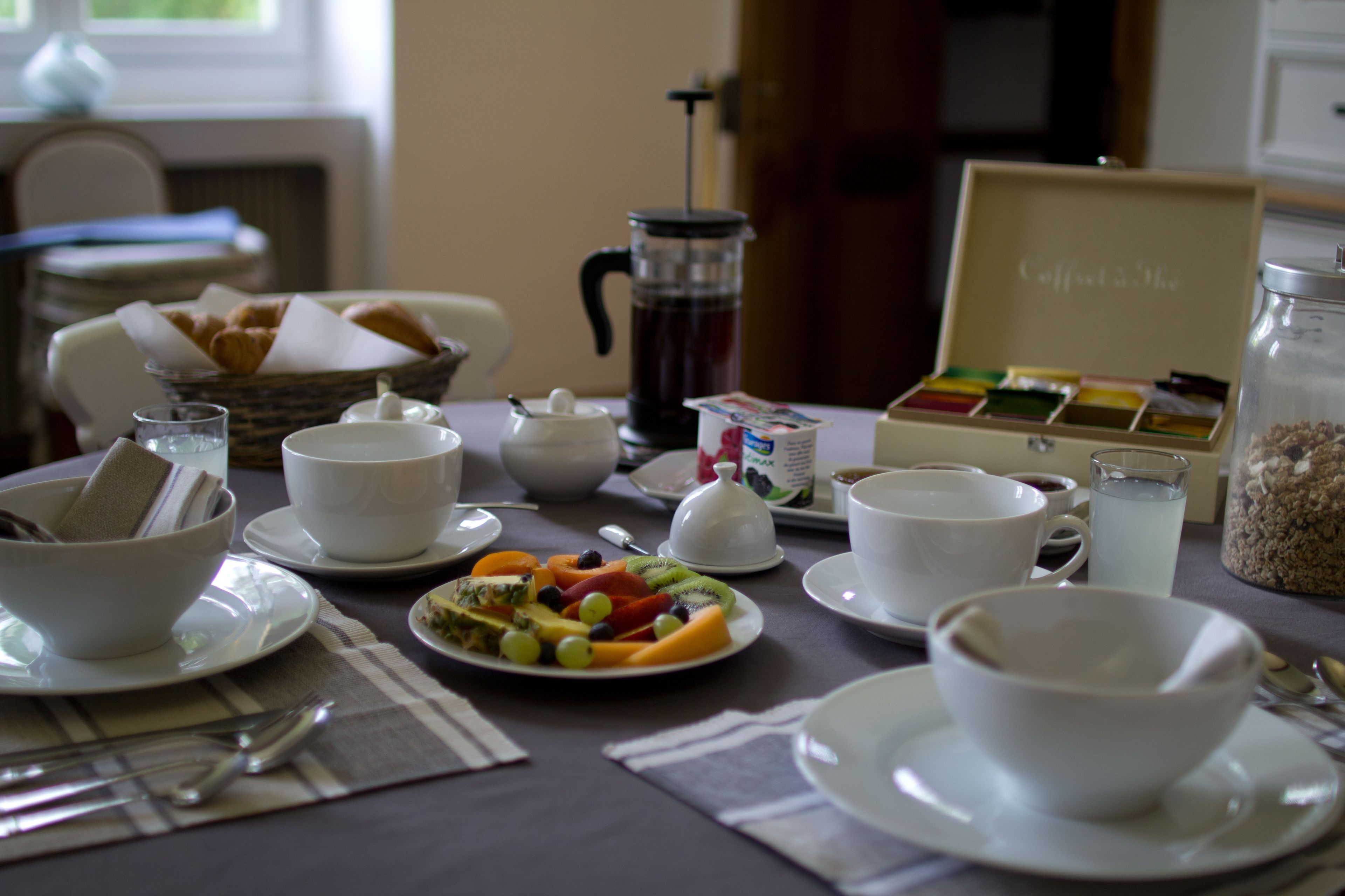 A breakfast setting with a coffee maker, a fruit plate, and a box of coffee and tea.