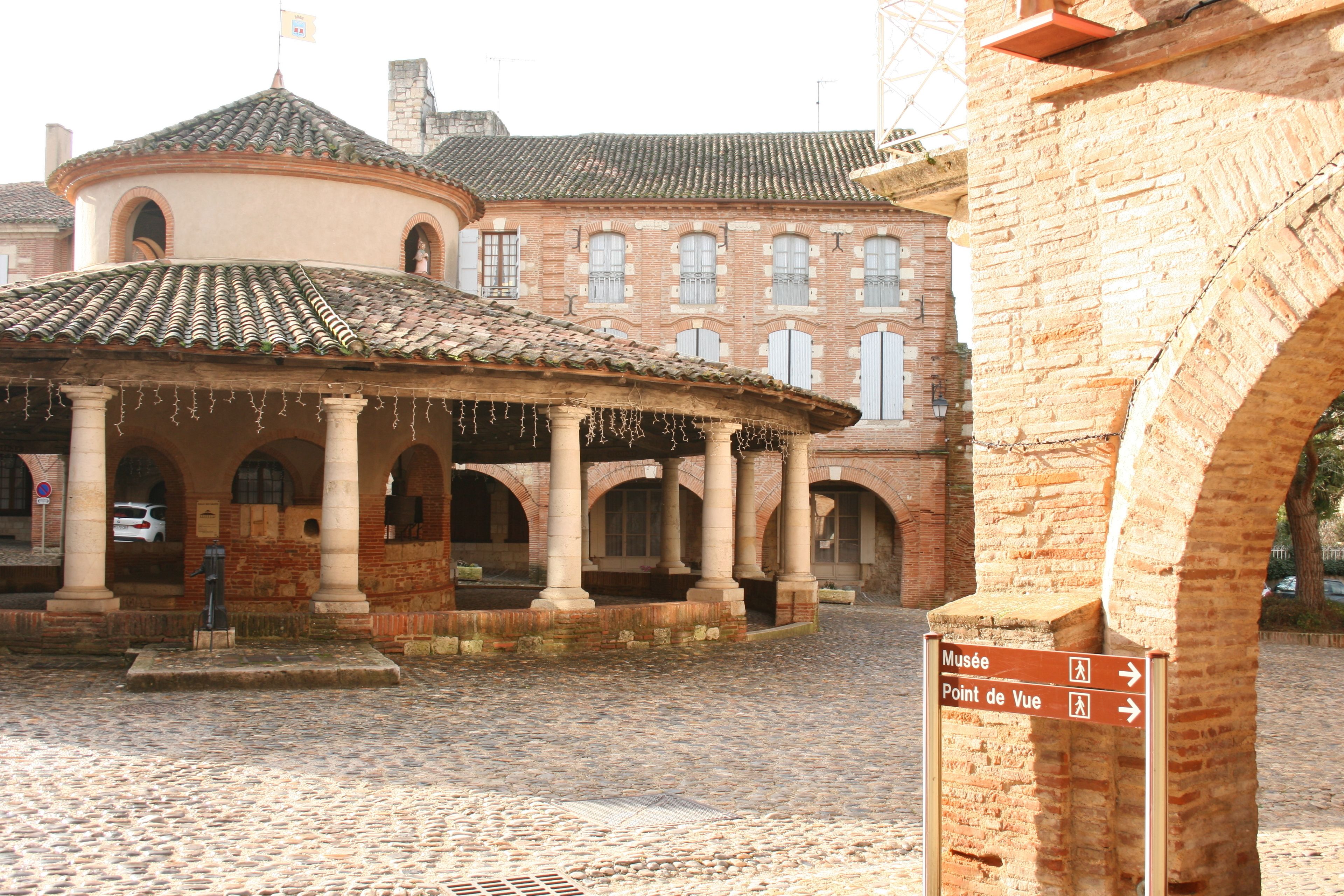 A cobblestone courtyard with a central pavilion and a building with arched windows in the background.