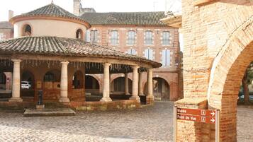 A cobblestone courtyard with a central pavilion and a building with arched windows in the background.
