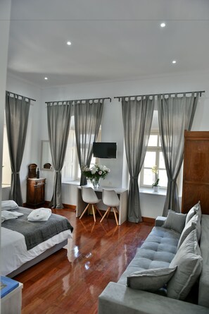 A hotel room with a bed, a sofa, a desk with a chair, a TV, and a window with curtains.