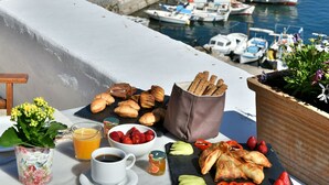 A breakfast setup with pastries, fruits, and coffee on a balcony overlooking a harbor with boats and buildings. - Douskos Port House (Hydra)